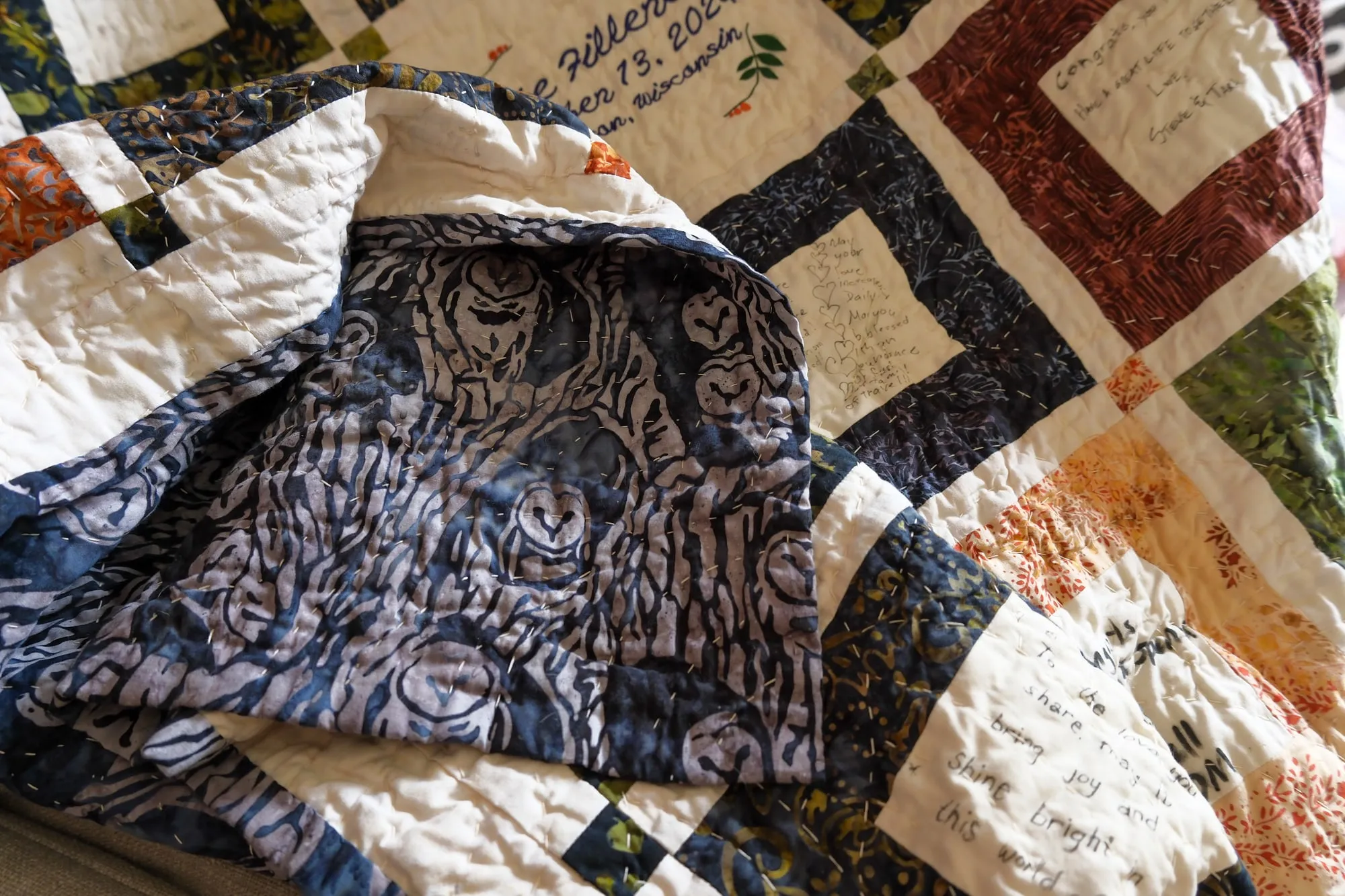 The corner of the quilt folded back to show the navy and grey batik backing, with rows of large hand-quilting stitches visible across both sides.